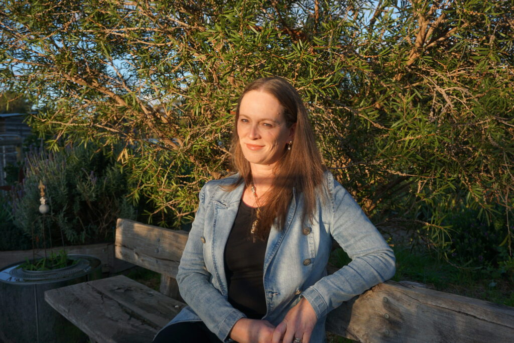 Melinda Charlesworth - Writer sits in front of a tree in the sunshine.